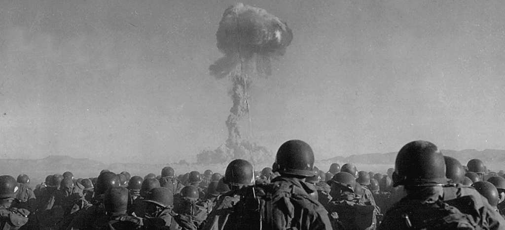 A group of Soldiers look on at a mushroom cloud from a nuclear bomb test.