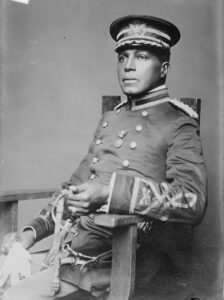 Soldier in early 20th century dress uniform wearing a medal in the middle of his chest. Seated, looking to the left. 