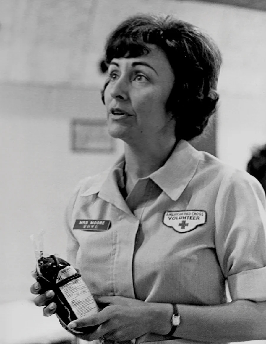 Woman in Redcross uniform holding a bag of fluid and looking to the left. 