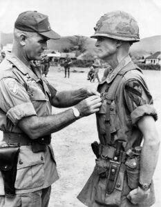 Soldier,left, wearing jungle fatigues pins a medal on the chest of a Soldier, also in jungle fatigues, standing at attention on the right. 